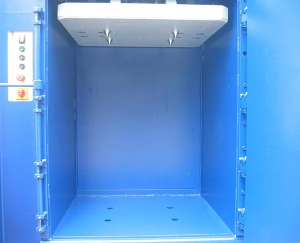 Interior shot of the FP200. The compacting press at the top is grey with four spikes pointing downward in a square formation, lining up with the four holes at the base of the compartment. A panel of five buttons and a switch can be seen to the left.