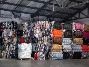 Stacks of baled clothing in a warehouse. Different materials and colours are squashed into large cube bales.